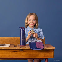 Young girl sitting at a desk with the BBox Harry Potter lunchbox and matching Harry Potter water bottle, smiling against a blue background