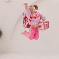 Child in pink and red striped outfit with matching Fox & Fallow Backpack, jumping .