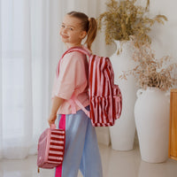 Young girl with a Fox and Fallow Burgundy striped backpack and small bag indoors.