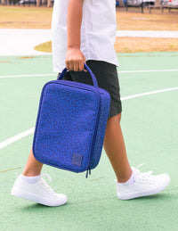 A child walking on a green outdoor court carrying a Montii Large Lunchbag with a top handle.