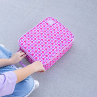 A Queen of Hearts Montii Large Insulated Lunchbag, being held by a child sitting on a gray concrete surface.
