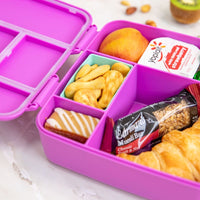 Montii Feast lunchbox with snacks including cookies, a yogurt bar, and a granola bar on a white surface.