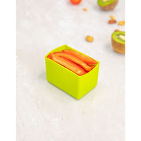 Montii Matcha Feast Cup with sliced carrots on a light surface with fruits in the background