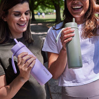 Two women holding the Lilac Love BBox Drink Bottle and the Olive BBox Flip Top Drink bottle outdoors