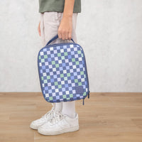 Child holding the Montii Checkmate Large Insulated Lunchbag on a wooden floor with a white wall background